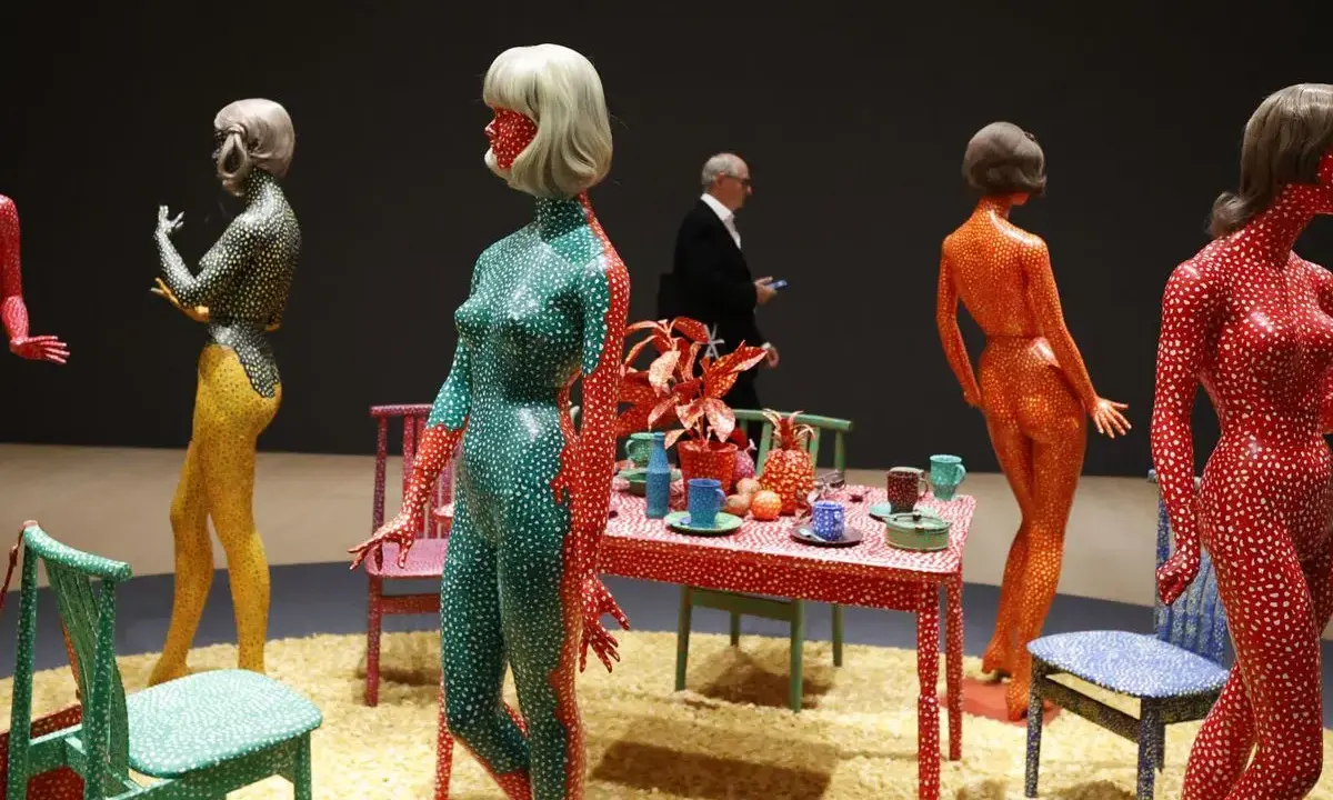Figuras humanas cubiertas de lunares, parte de las **obras de arte de Yayoi Kusama**, junto a una mesa con objetos decorativos.