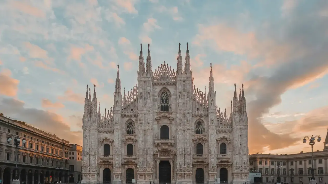 La majestuosa Catedral de Milán, una de las más impresionantes catedrales del mundo, se alza bajo un cielo crepuscular con nubes rosadas.