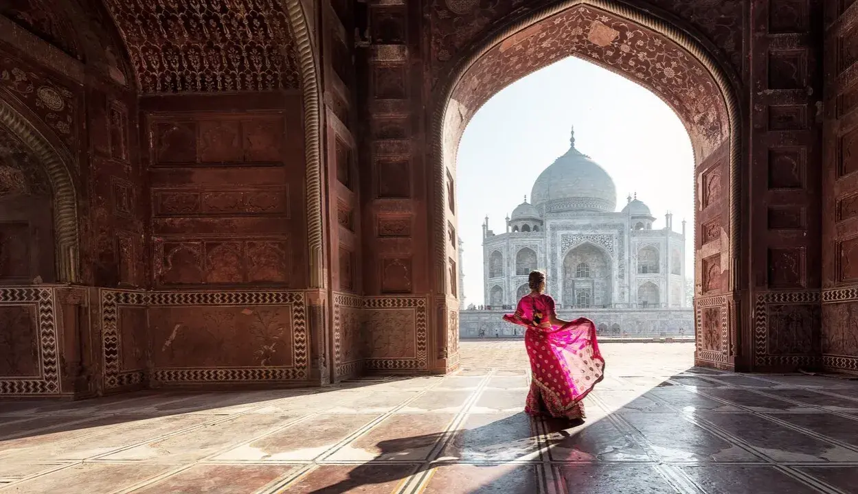Una mujer con un sari rosa vibrante baila bajo un arco, revelando el Taj Mahal. Descubre curiosidades del Taj Mahal.
