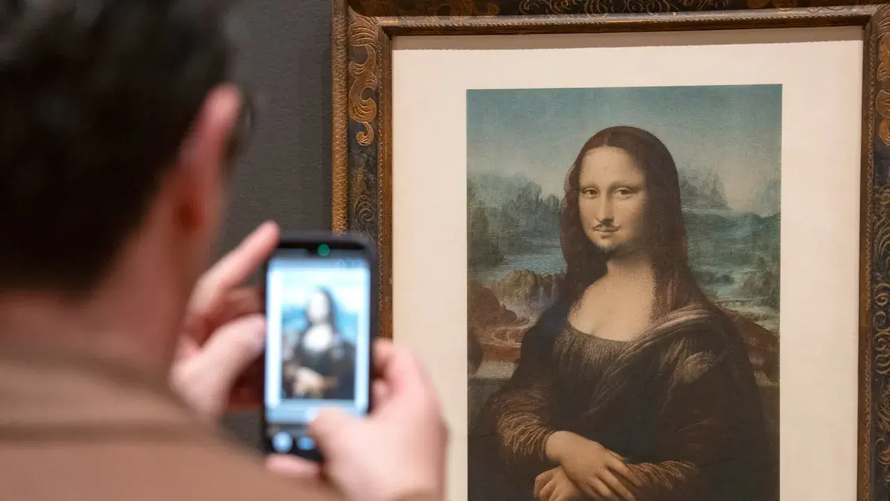Un visitante fotografía la Mona Lisa con bigote y perilla, una de las obras de arte de Marcel Duchamp, en un museo.