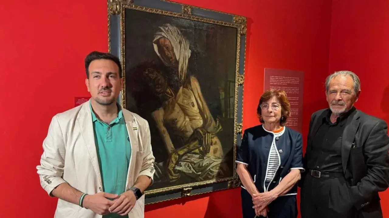 Baldomero Romero Ressendi, junto a dos personas, posa ante un cuadro de temática religiosa en una sala de museo.