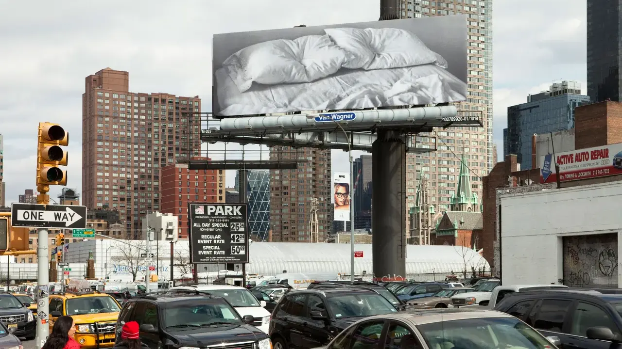 Un cartel de Felix Gonzalez Torres con sábanas arrugadas preside una calle de Nueva York, rodeado de tráfico y edificios.