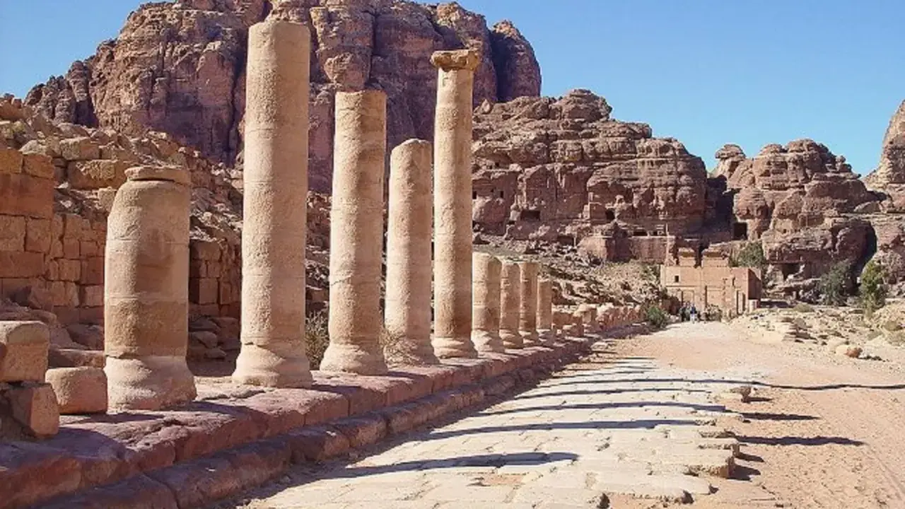 Columnas antiguas en Petra, una de las 7 maravillas del mundo, flanquean un camino de piedra bajo un cielo azul.