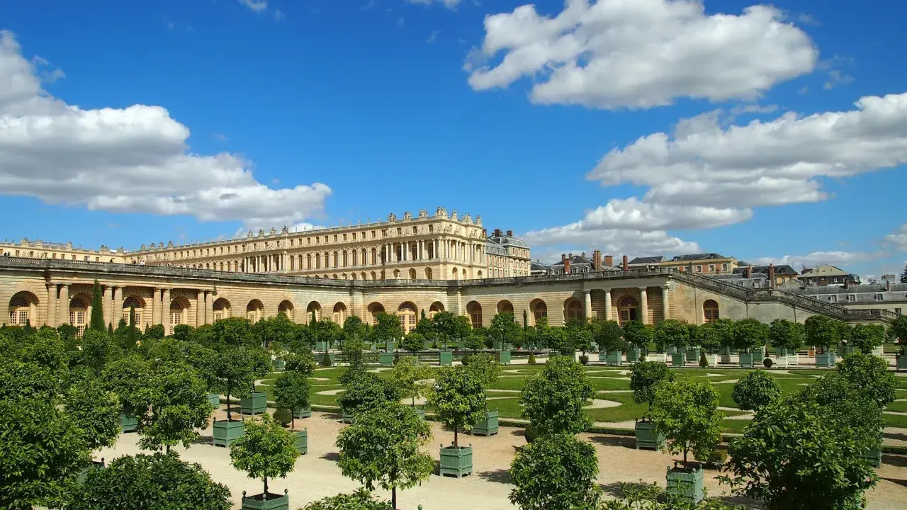 Jardines del Palacio de Versalles, un lugar lleno de curiosidades, con árboles en macetas y un cielo azul con nubes.