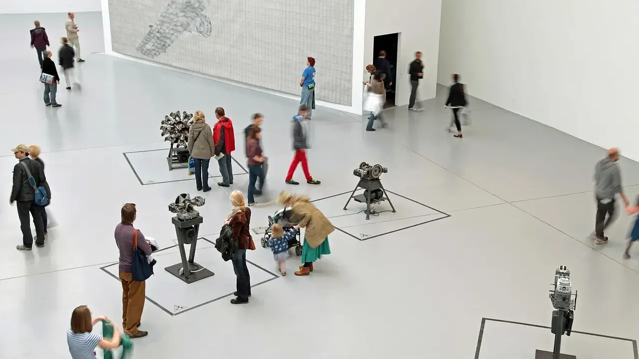 Gente pasea por una galería de arte, observando instalaciones mecánicas y un gran mural. Un día en las ferias de arte.