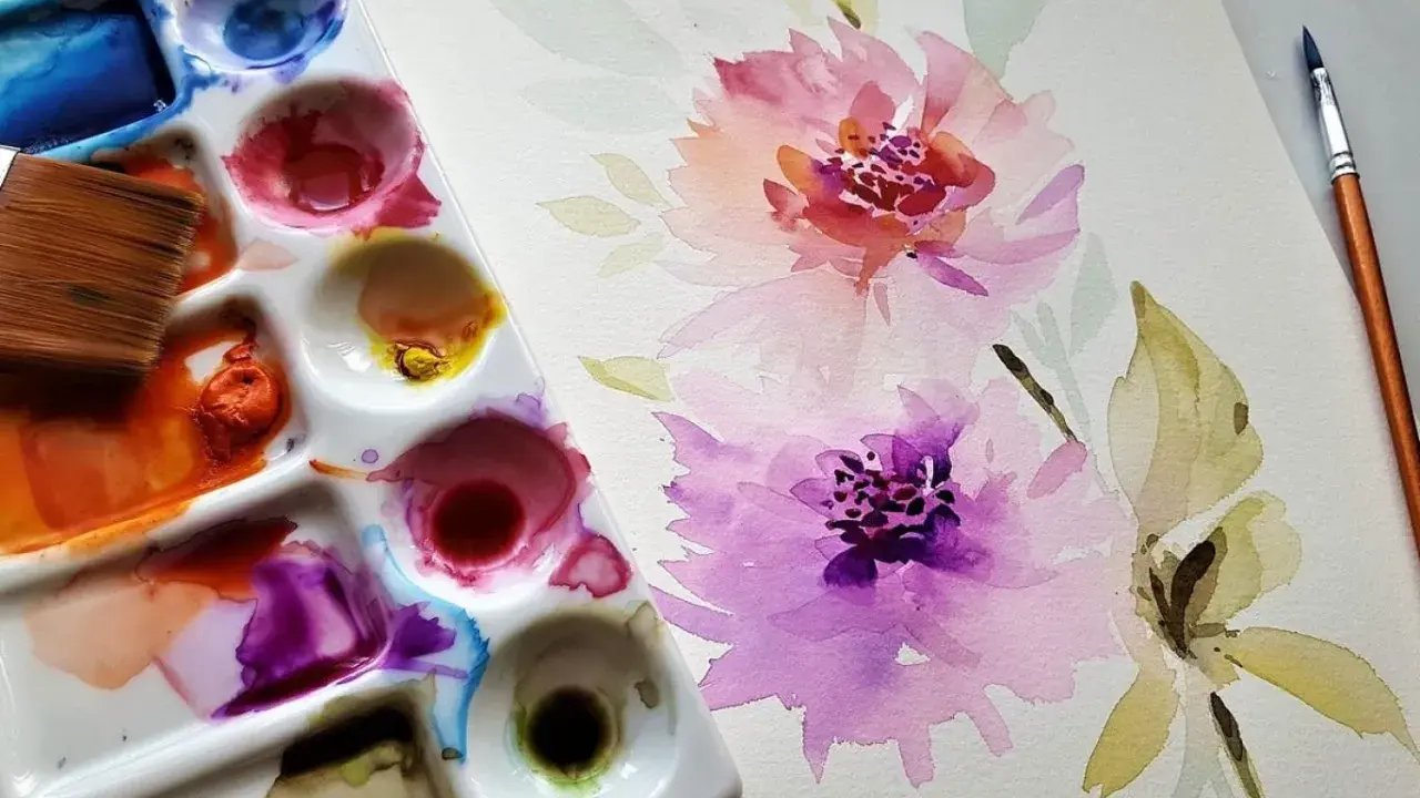 Paleta de acuarelas con pincel y flores en proceso. Inspiración para pintar con acuarelas.