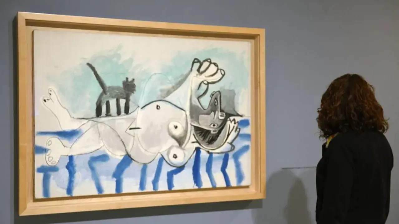 Una mujer observa una pintura de **Pablo Picasso** con una figura tumbada y un gato.