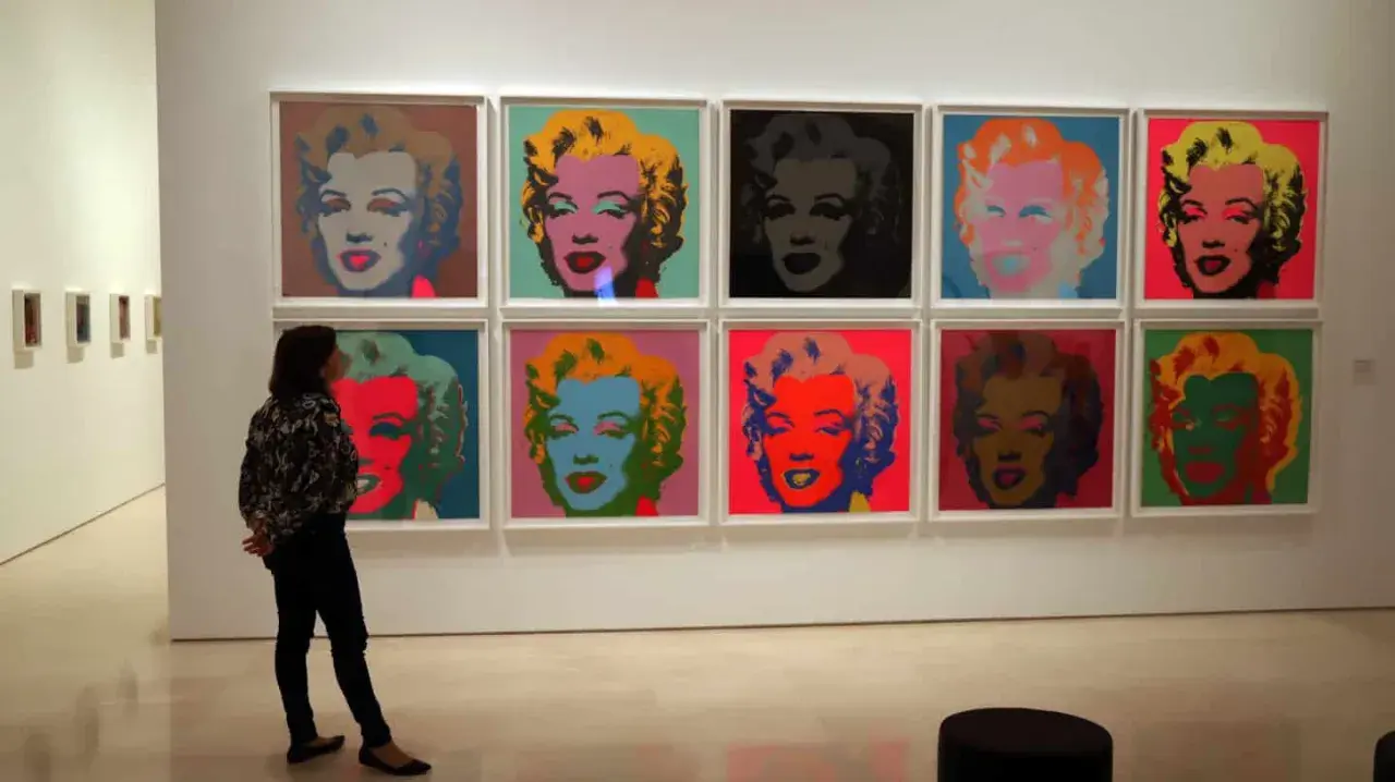 Una persona observa la icónica serie de Marilyn de Andy Warhol, con retratos vibrantes en colores pop.