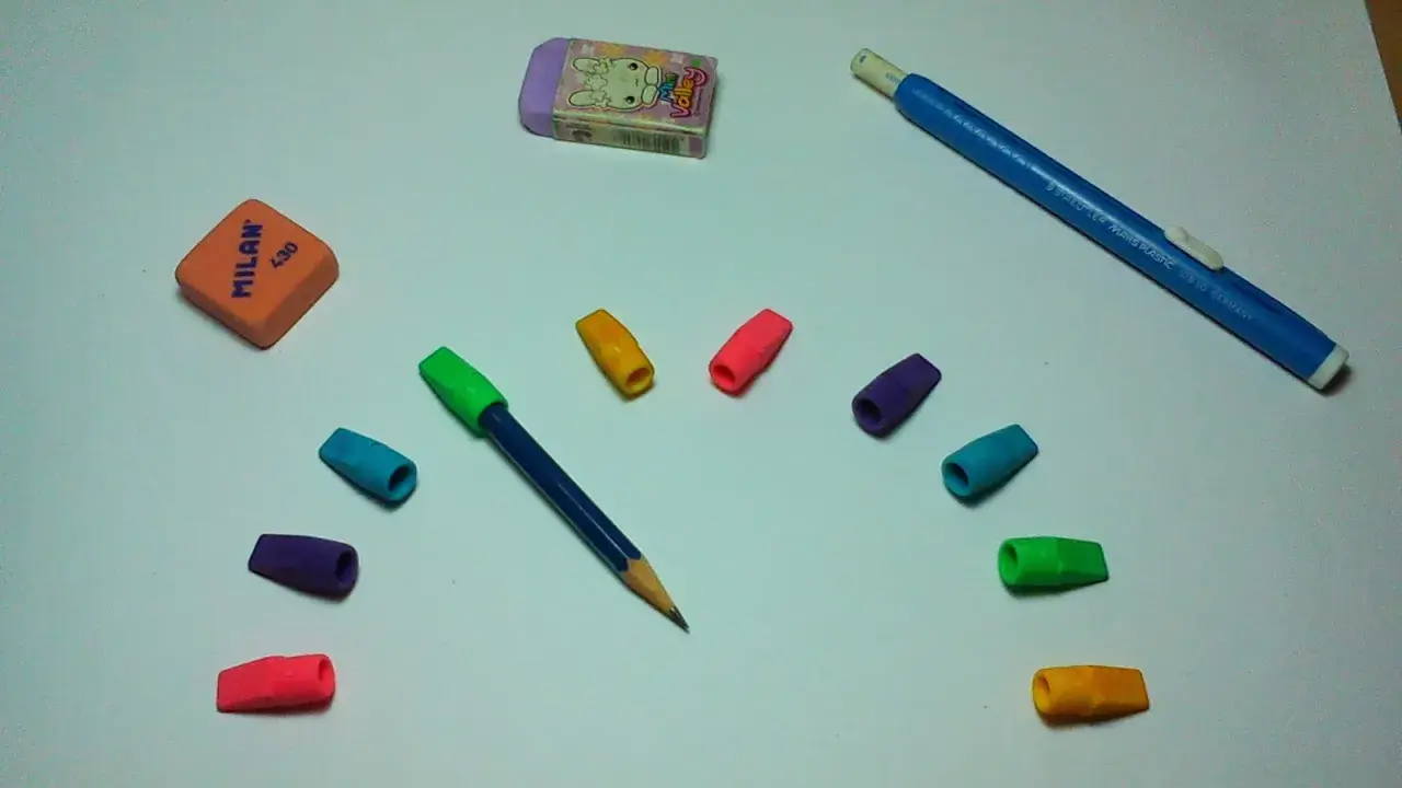 Un lápiz azul con goma de borrar de colores y dos gomas de borrar, una naranja y otra morada con un conejo, listas para un dibujo.