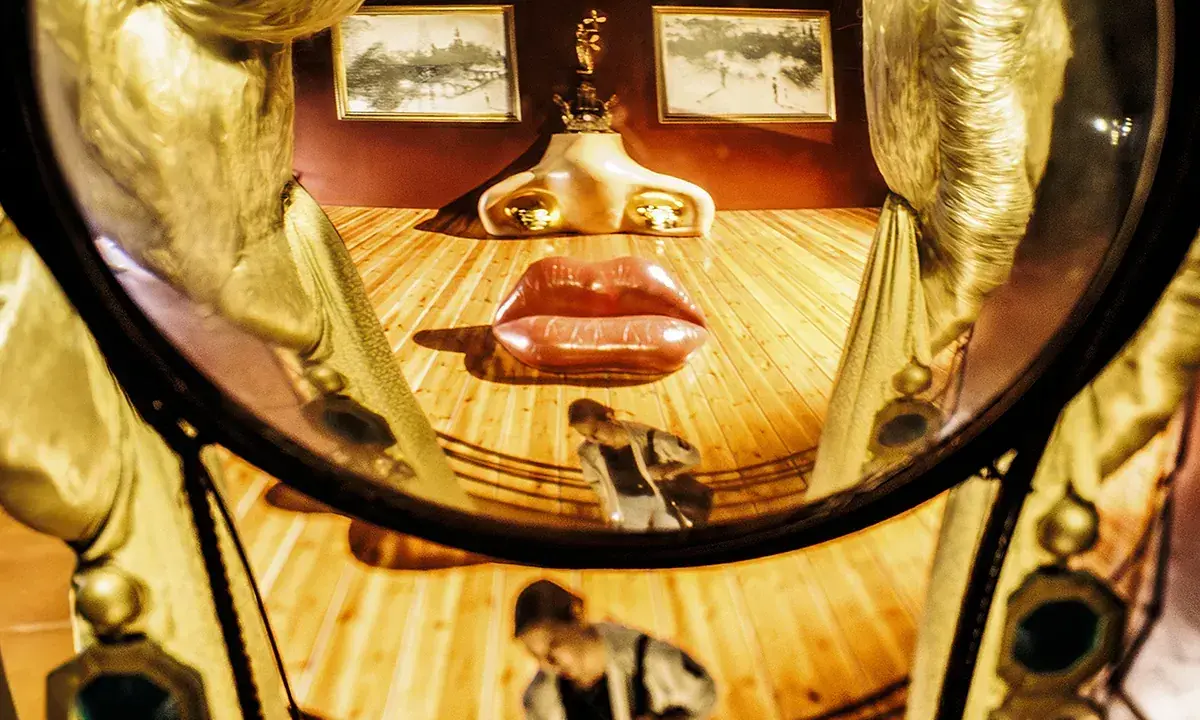 El rostro de Mae West de Dalí, con labios rojos y nariz dorada, se refleja en un espejo curvo.