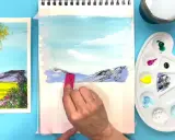 Creando dibujos de paisajes fáciles. Una mano aplica pintura a un lienzo con montañas y cielo azul.