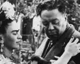 Frida Kahlo y Diego Rivera, una pareja icónica, comparten un momento íntimo. Frida, con flores en el cabello, mira a Diego, quien parece reflexivo.