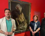 Baldomero Romero Ressendi, junto a dos personas, posa ante un cuadro de temática religiosa en una sala de museo.
