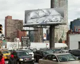 Un cartel de Felix Gonzalez Torres con sábanas arrugadas preside una calle de Nueva York, rodeado de tráfico y edificios.