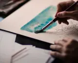 Una mano aplica acuarela sobre lienzo, dando vida a un boceto de barca con carga.