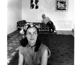 Françoise Gilot joven, con una corona de hojas, mira pensativa mientras Picasso descansa en el fondo, rodeados de sus obras.