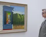 Un hombre contempla "Habitación de hotel" de Edward Hopper, una mujer mira por la ventana de una casa.