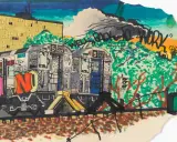 Un tren del metro cubierto de grafitis, un capítulo vibrante de la historia del graffiti, avanza bajo un cielo nublado.
