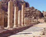 Columnas antiguas en Petra, una de las 7 maravillas del mundo, flanquean un camino de piedra bajo un cielo azul.