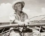 Un viejo pescador con sombrero de paja rema en su bote, evocando el espíritu de "el viejo y el mar resumen".