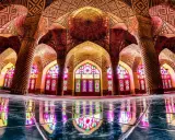 Interior de la mezquita Nasir ol Molk, con arcos intrincados, columnas retorcidas y vitrales de colores que proyectan un caleidoscopio de luz sobre el suelo pulido.