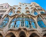 Fachada de edificio **art nouveau** con balcones curvos y vidrieras de colores, reflejando el cielo azul y árboles.