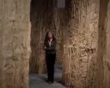 Cristina Iglesias, rodeada de imponentes estructuras de madera que evocan un bosque, contempla la obra.
