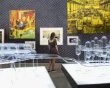 Una curadora de arte observa una instalación de vidrio y pinturas abstractas en una galería.