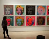 Una persona observa la icónica serie de Marilyn de Andy Warhol, con retratos vibrantes en colores pop.