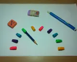 Un lápiz azul con goma de borrar de colores y dos gomas de borrar, una naranja y otra morada con un conejo, listas para un dibujo.