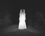 Una figura espectral con un vestido blanco aparece en un camino oscuro, perfecta para cuentos de terror cortos.