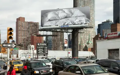 Un cartel de Felix Gonzalez Torres con sábanas arrugadas preside una calle de Nueva York, rodeado de tráfico y edificios.