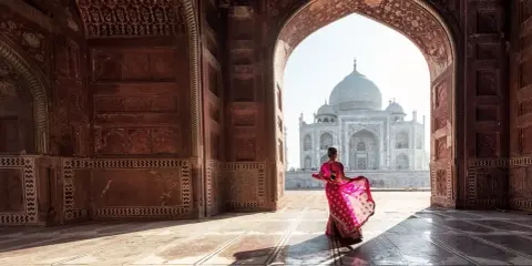 Una mujer con un sari rosa vibrante baila bajo un arco, revelando el Taj Mahal. Descubre curiosidades del Taj Mahal.