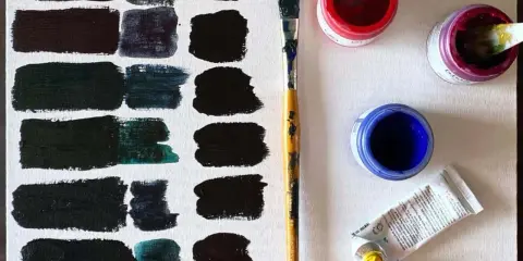 Pinceles y botes de pintura roja, azul y morada sobre lienzo, explorando como se hace el color negro con diferentes tonos.