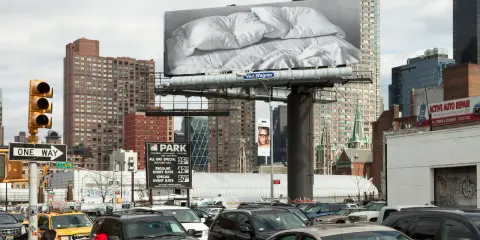 Un cartel de Felix Gonzalez Torres con sábanas arrugadas preside una calle de Nueva York, rodeado de tráfico y edificios.