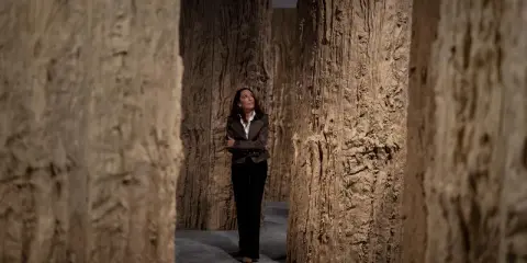 Cristina Iglesias, rodeada de imponentes estructuras de madera que evocan un bosque, contempla la obra.