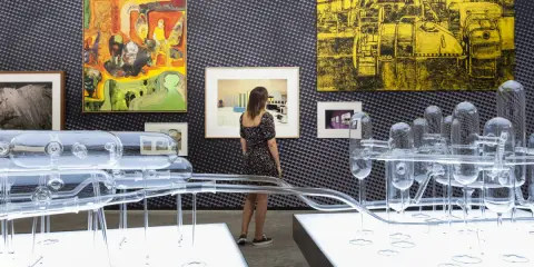 Una curadora de arte observa una instalación de vidrio y pinturas abstractas en una galería.