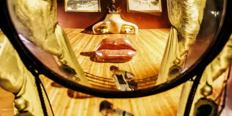 El rostro de Mae West de Dalí, con labios rojos y nariz dorada, se refleja en un espejo curvo.