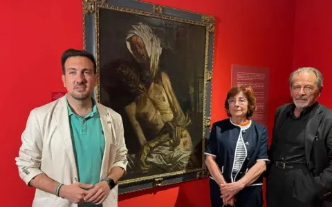 Baldomero Romero Ressendi, junto a dos personas, posa ante un cuadro de temática religiosa en una sala de museo.