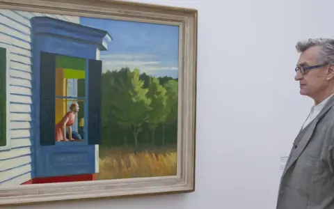 Un hombre contempla "Habitación de hotel" de Edward Hopper, una mujer mira por la ventana de una casa.