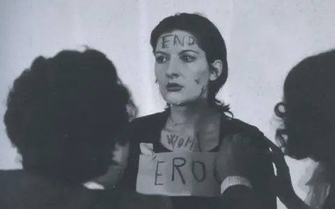 Marina Abramović en "Rhythm 0", con "END" escrito en su frente y "WOMAN ERO" en su pecho.