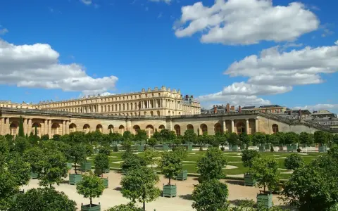 Jardines del Palacio de Versalles, un lugar lleno de curiosidades, con árboles en macetas y un cielo azul con nubes.