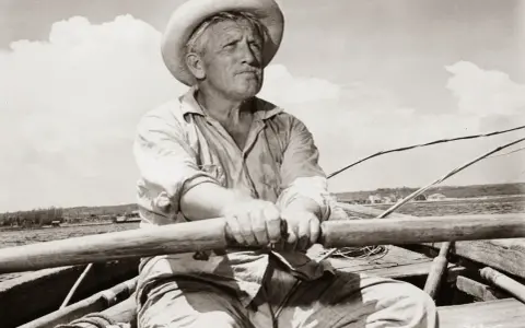 Un viejo pescador con sombrero de paja rema en su bote, evocando el espíritu de "el viejo y el mar resumen".