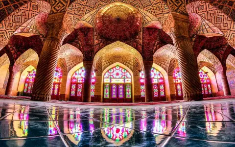 Interior de la mezquita Nasir ol Molk, con arcos intrincados, columnas retorcidas y vitrales de colores que proyectan un caleidoscopio de luz sobre el suelo pulido.