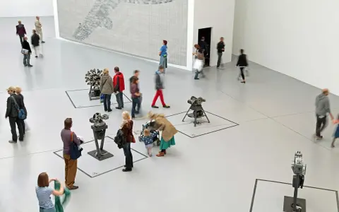 Gente pasea por una galería de arte, observando instalaciones mecánicas y un gran mural. Un día en las ferias de arte.