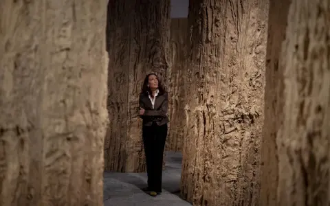 Cristina Iglesias, rodeada de imponentes estructuras de madera que evocan un bosque, contempla la obra.