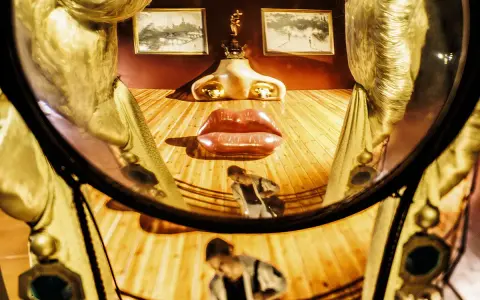 El rostro de Mae West de Dalí, con labios rojos y nariz dorada, se refleja en un espejo curvo.