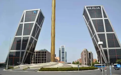 Dos icónicas estructuras diseñadas por Santiago Calatrava se alzan inclinadas, flanqueando una columna dorada.