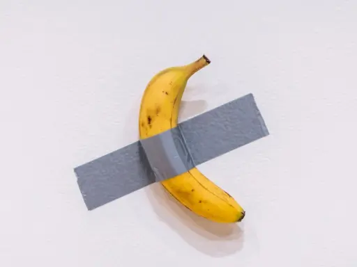 Una obra de arte platano, un plátano amarillo pegado a una pared blanca con cinta adhesiva gris.