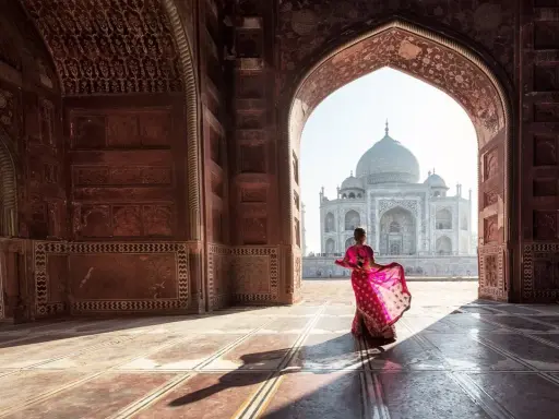 Una mujer con un sari rosa vibrante baila bajo un arco, revelando el Taj Mahal. Descubre curiosidades del Taj Mahal.